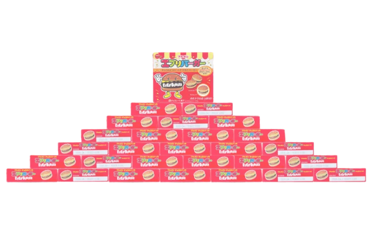 エブリバーガーの赤いパッケージをピラミッド状に積み上げた構成。ミニチョコバーガーの箱が階段状に並び、家庭内で撮影された遊び心のある構図となっている。